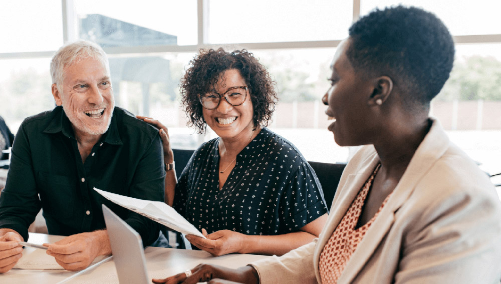 3 business colleagues smiling at meeting table